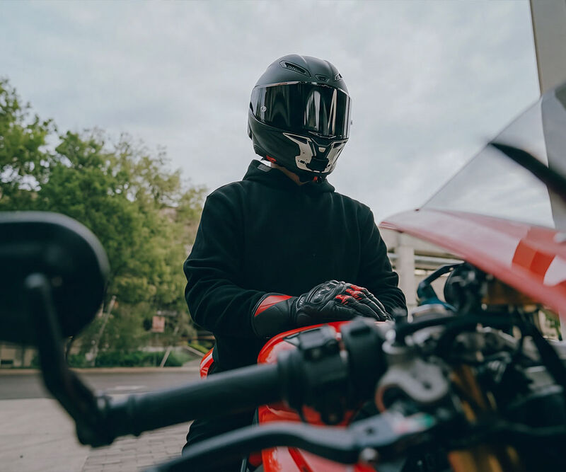 Motociclista con casco y guantes de protección apoyado en una moto deportiva roja